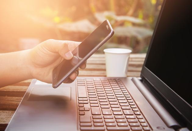 Hand holding a phone in front of a laptop